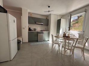 Eine Küche mit weißen Geräten, einem Esstisch mit Stühlen und Blick durch ein Fenster.