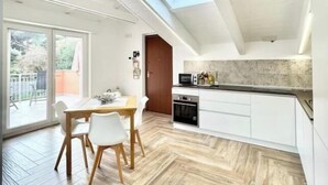 A modern kitchen with a skylight, wooden flooring, and a dining area with a table and chairs. - Hostdomus - Bellavista Suite (Pietra Ligure)