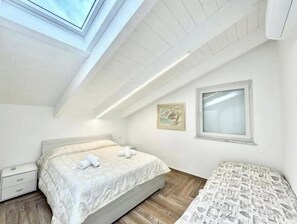 Une chambre à coucher avec un puits de lumière, un lit, une table de chevet, une fenêtre et une œuvre d’art accrochée au mur.