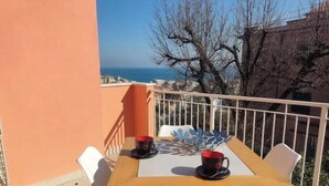 A wooden table with two chairs and a red cup on a balcony with a view of the sea. - Hostdomus - Bellavista Suite (Pietra Ligure)
