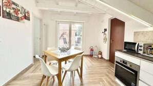 A modern kitchen with a microwave, oven, and dining area with a table and chairs. - Hostdomus - Bellavista Suite (Pietra Ligure)