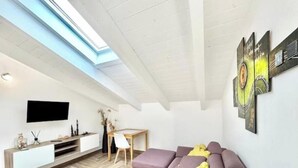 A modern living room with a sofa, a TV, a desk, and artwork on the wall. - Hostdomus - Bellavista Suite (Pietra Ligure)