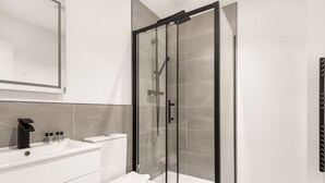 Een moderne badkamer met een douchecabine van glas, een witte wastafel en een toilet.