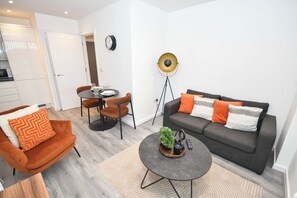 A modern living room with a sofa, armchair, coffee table, and a dining area with chairs and a table. - Bright & Contemporary 1 Bed Apartment in Leeds (Leeds)