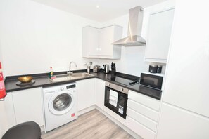 A compact kitchen with a washing machine, a sink, a stove, and a microwave. - Bright & Contemporary 1 Bed Apartment in Leeds (Leeds)