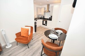 Cozinha compacta com eletrodomésticos modernos, sala de jantar com duas cadeiras e uma mesa pequena posta para dois.
