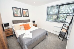 Quarto com cama, mesas de cabeceira, janela com persianas e espelho.
