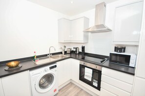 A compact kitchen with white cabinets, a built-in washing machine, a microwave, and a coffee machine. - Bright & Contemporary 1 Bed Apartment in Leeds (Leeds)