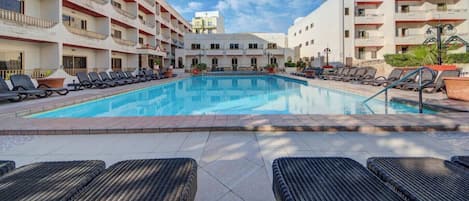 A swimming pool with lounge chairs and a building with balconies.