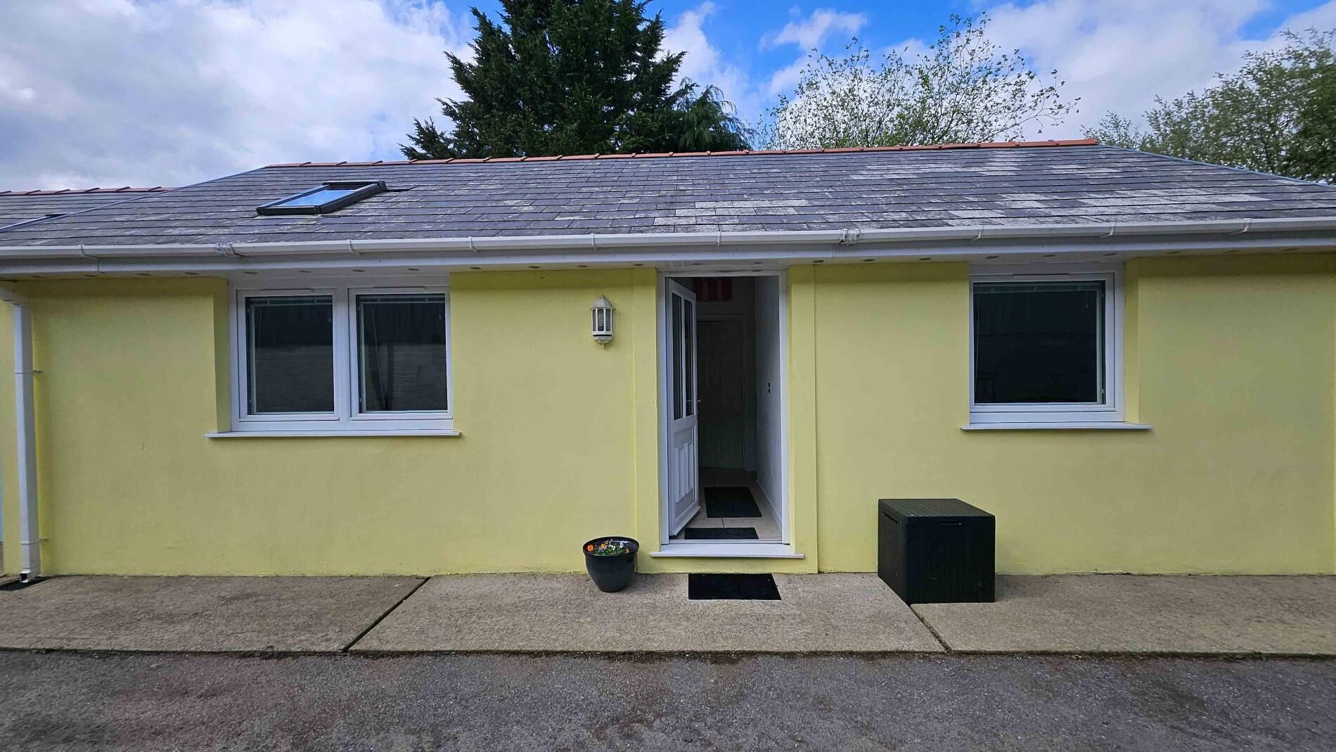 Un bâtiment jaune avec une porte, des fenêtres, un petit espace extérieur et un panneau solaire sur le toit.