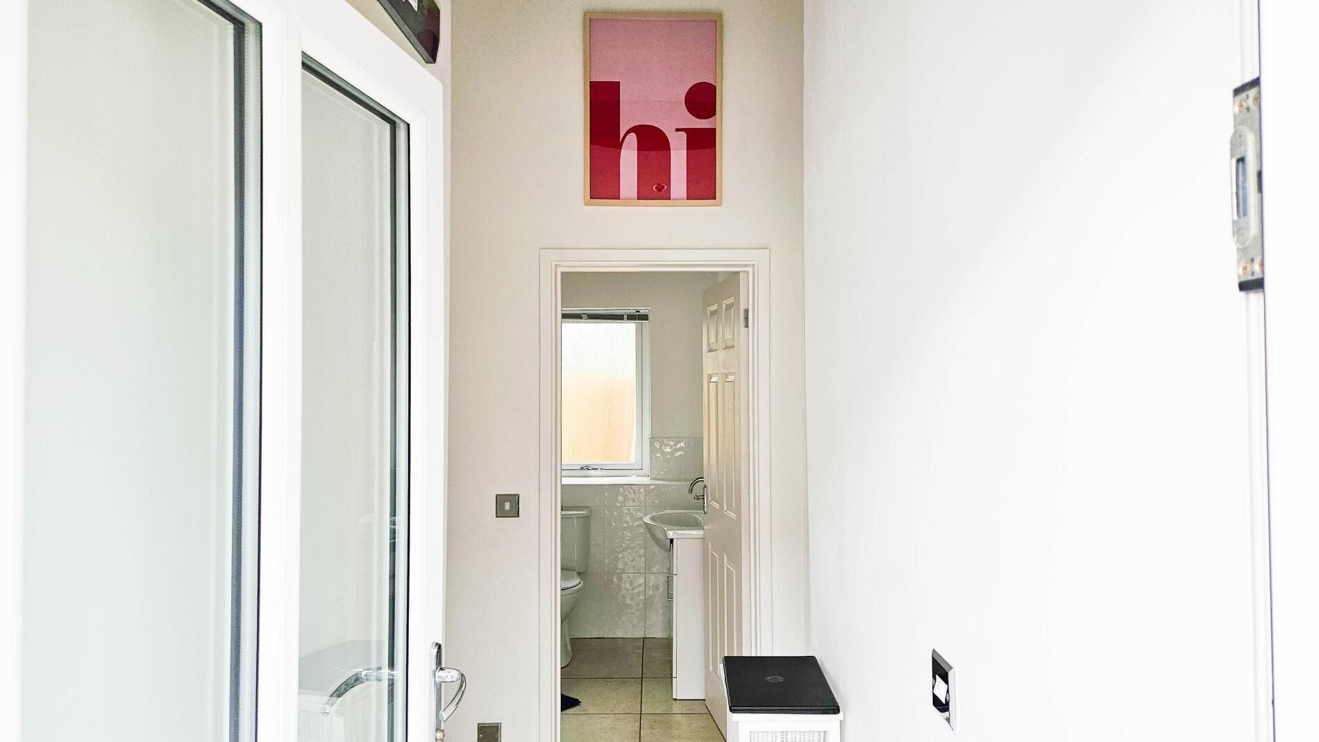A hallway leading to a bathroom with a toilet, sink, and a window.