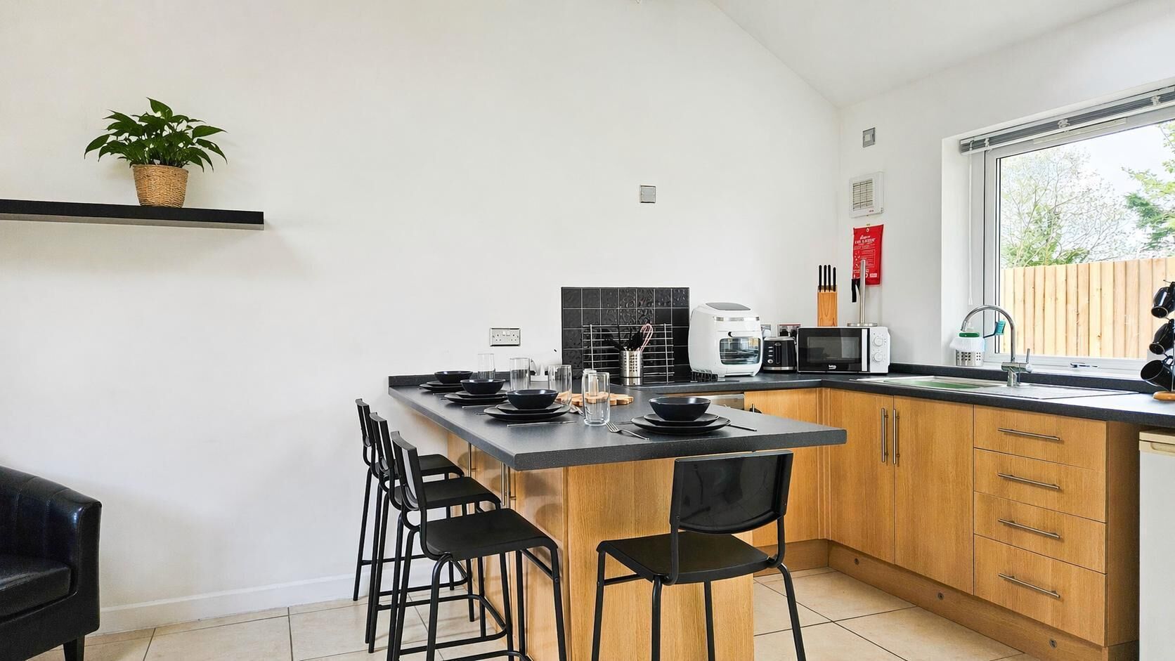 Una cocina moderna con una isla central, taburetes negros tipo barra, una planta en maceta y un ventanal con vistas.