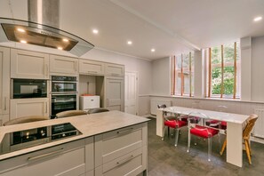 A modern kitchen with built-in appliances, a dining area with a white table and red chairs, and large windows with blinds. - Finest Retreats | Wallingbrook Lodge (Chulmleigh)