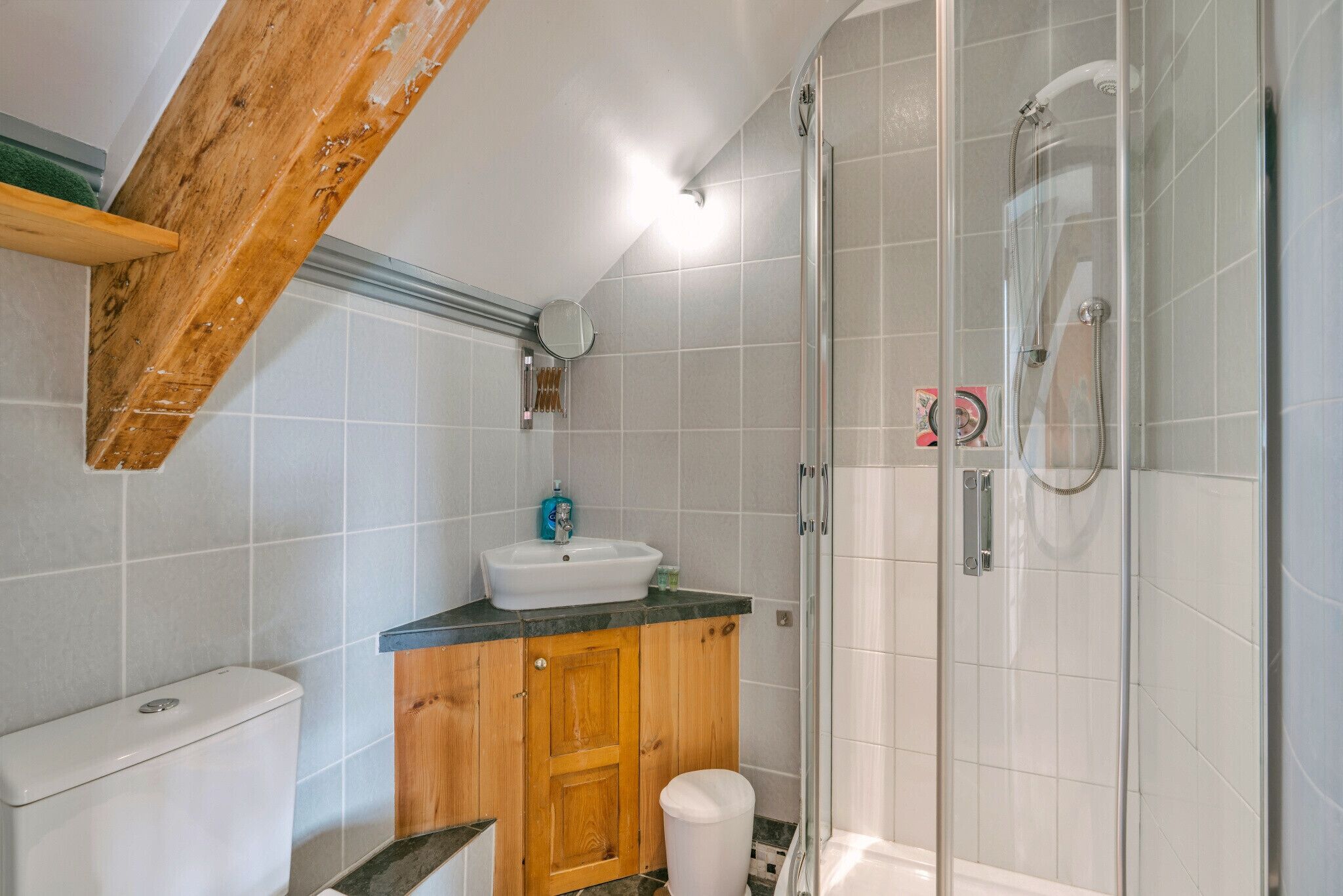 Une salle de bain comprenant des toilettes, un lavabo, un meuble en bois et une douche fermée par des parois en verre.
