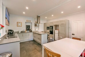 A modern kitchen with a central island, built-in oven, and a dining area with a white table. - Finest Retreats | Wallingbrook Lodge (Chulmleigh)