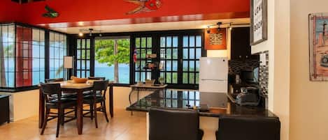 A kitchen with a view of the sea, a dining area with chairs, and a bar with stools.