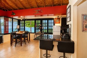 A kitchen with a view of the sea, a dining area with chairs, and a bar with stools. - Tropical SeaSide Villa (Aguada)