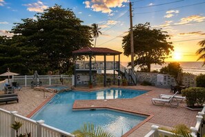 A swimming pool with a gazebo, lounge chairs, and a view of the sunset over the ocean. - Tropical SeaSide Villa (Aguada)