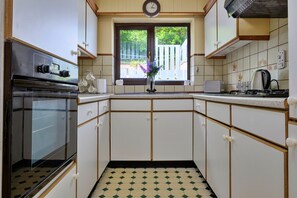 A kitchen with a stove, oven, and window with a view of a fence. - Finest Retreats | Delfryn (Talysarn)