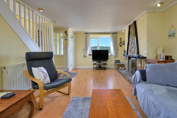 A living room with a wooden staircase, a flat-screen TV, a fireplace, and a sofa. - Finest Retreats | Delfryn (Talysarn)