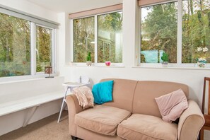 A room with a beige sofa, a white desk, and a window with a view of trees. - Arfron (Dinas Cross)