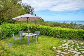 A table with chairs and an umbrella in a garden with a view of the sea. - Arfron (Dinas Cross)