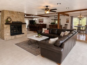 A spacious living room with a stone fireplace, leather sofa, and a dining area in the background. - Spacious Kilgore Home • Sleeps 14 • Near Downtown • Gatherings Welcome (Kilgore)