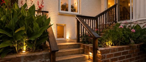 A house with a brick exterior, a wooden staircase, and a well-lit entrance.