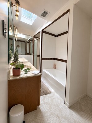 Ein modernes Badezimmer mit Badewanne, Waschtisch inklusive Spiegel und einer Topfpflanze.