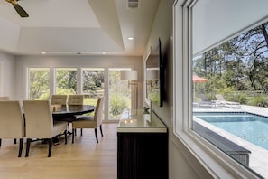 Un espace repas moderne avec une table en verre, des chaises et une vue sur une piscine extérieure.