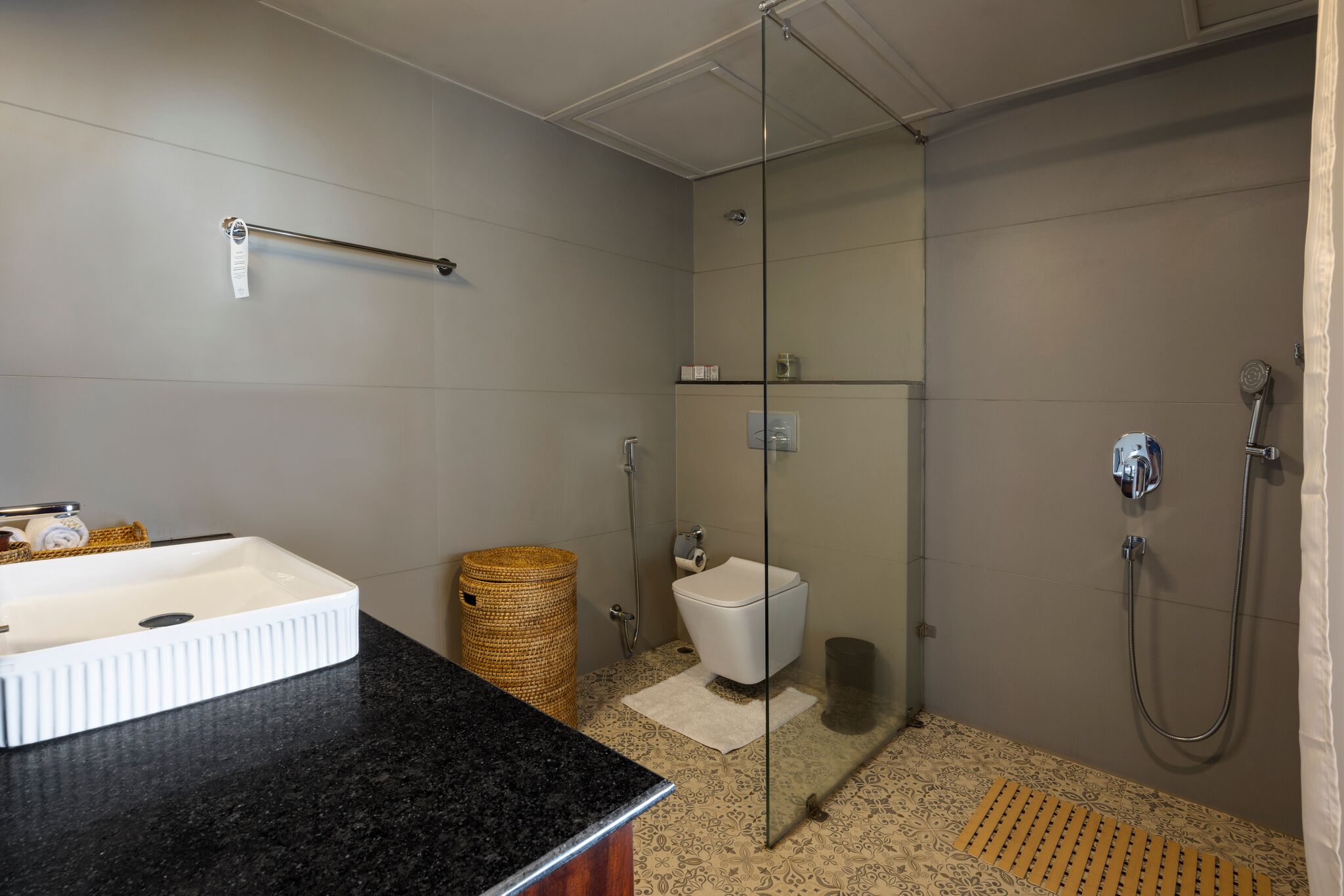 A bathroom with a glass-enclosed shower, a white toilet, a black countertop sink, and a woven basket.