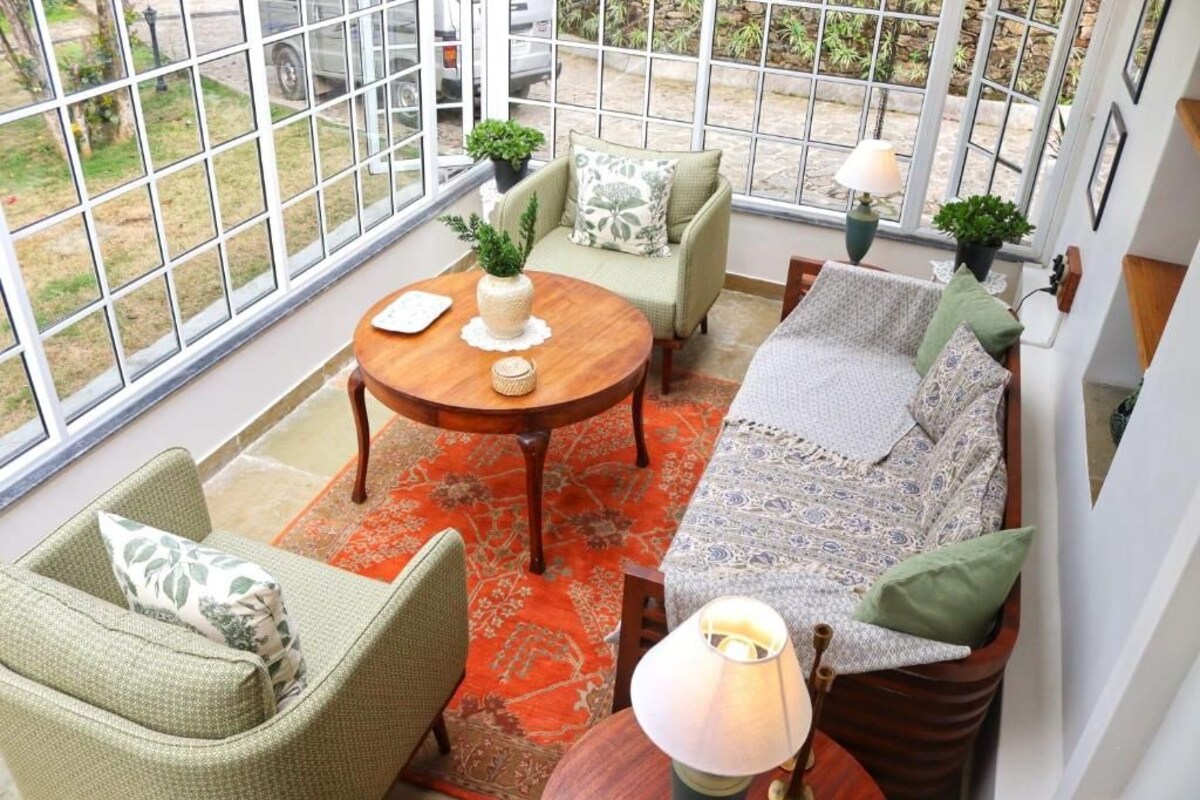 A cozy indoor space with a sofa, chairs, a table, and a view through large windows.