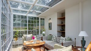 A conservatory with a glass ceiling, a round wooden table, and a sofa set. - Singell Tea Estate- CGH Earth Experience (Kurseong)