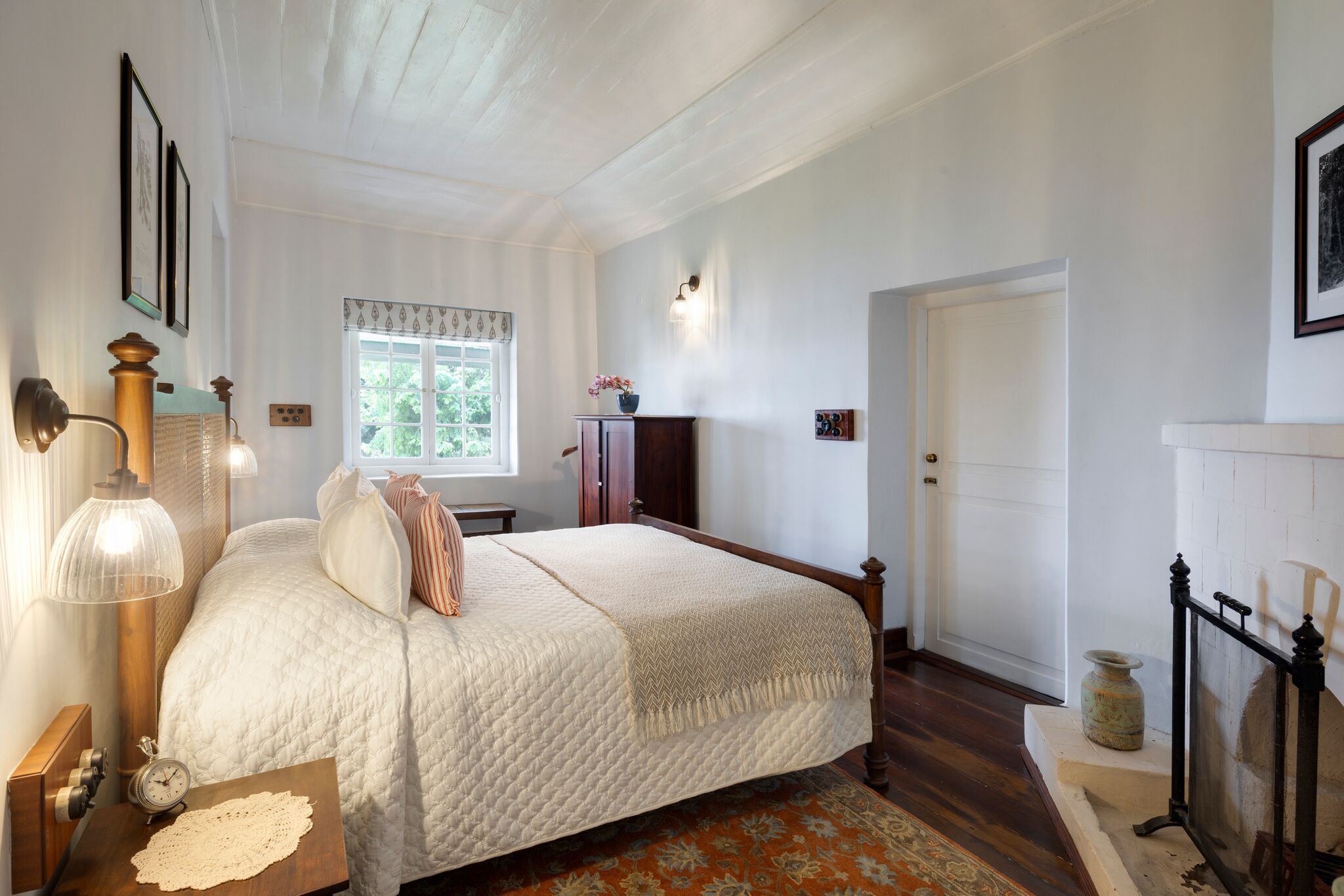 A bedroom with a bed, a nightstand, a lamp, a window, and a door.