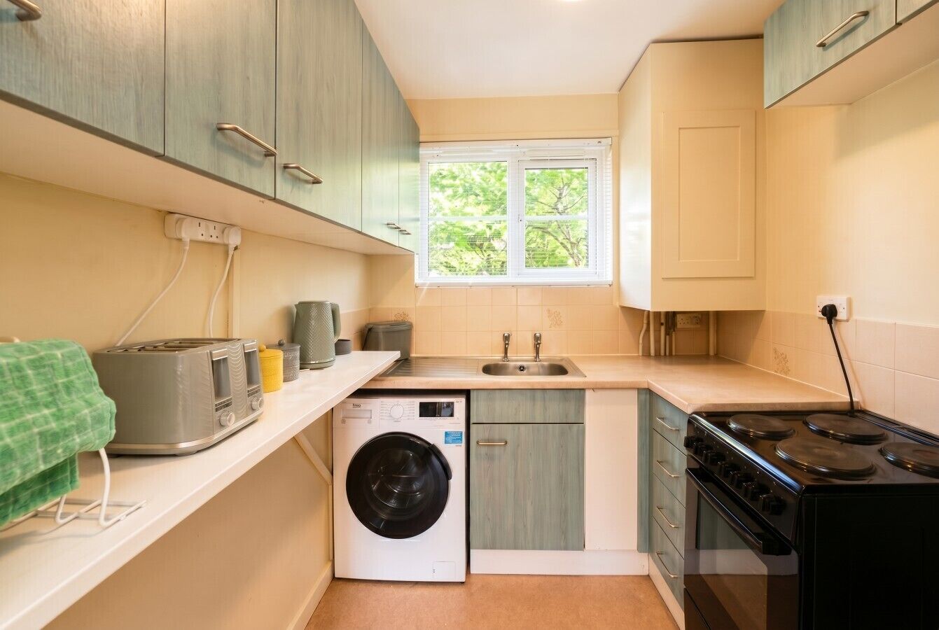 Une cuisine compacte équipée d’un lave-linge, d’une cuisinière et d’un évier.