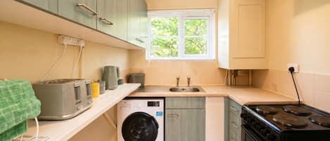 A compact kitchen with a washing machine, a stove, and a sink.