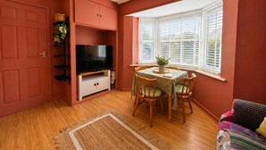 Una habitación con una mesa de comedor, sillas, un televisor, una ventana con persianas y una puerta.