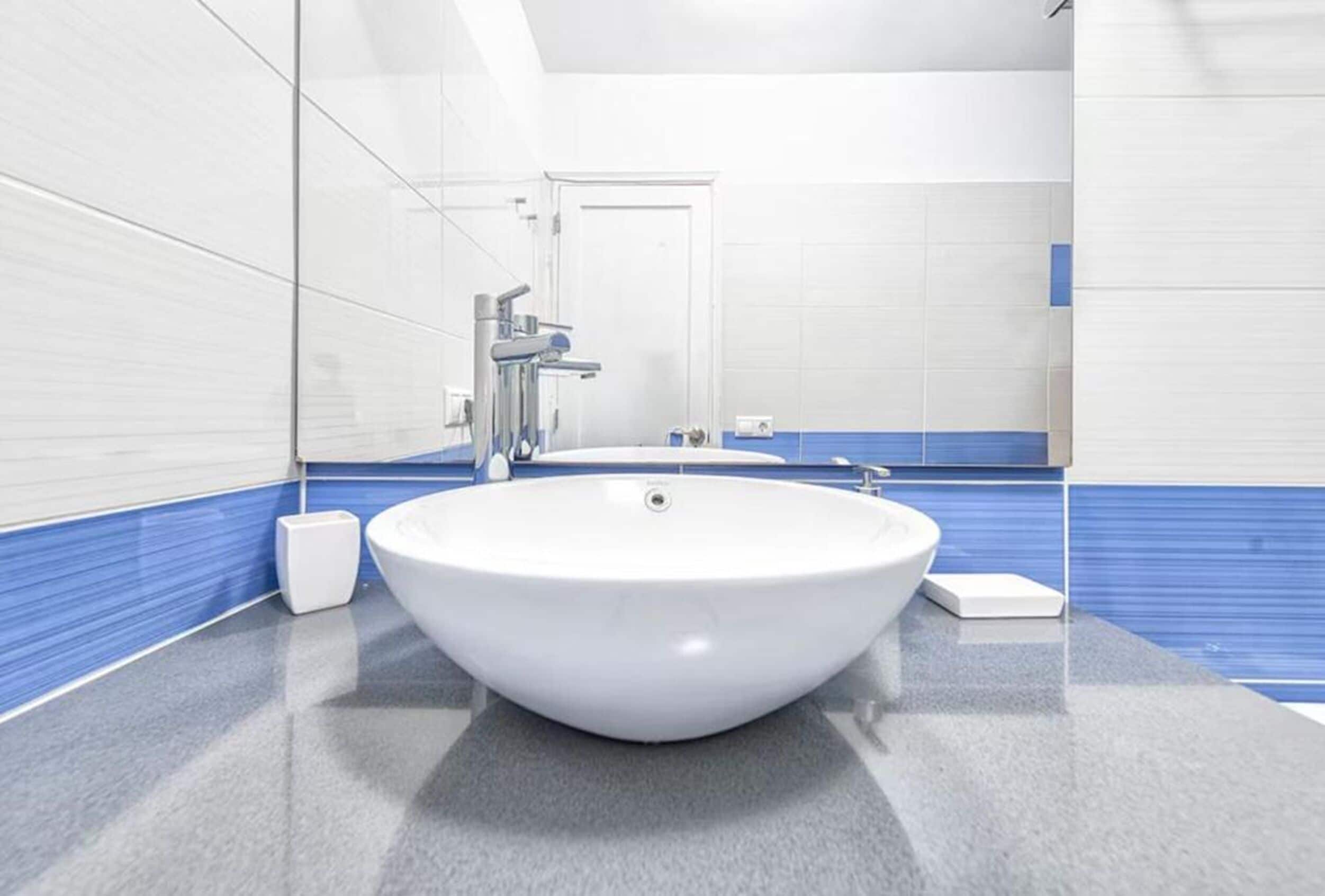 A modern bathroom with a large white sink, a mirror, and a door.