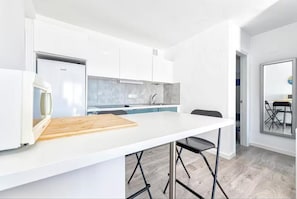 Une cuisine moderne avec des meubles blancs, un plan de travail blanc et une planche à découper en bois.