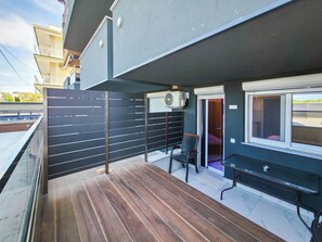Un balcón moderno al aire libre con piso de madera, cercado con una valla de metal negro, una silla y una mesa.