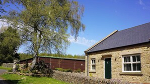 A stone building with a green door, a stone wall, and a tree in front. - 1 The Old Stables is a rural cottage with scenic countryside views. (Knitsley)