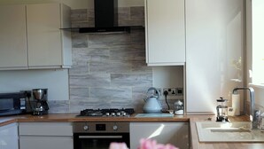 A modern kitchen with a stove, microwave, and coffee maker. There is a vase with flowers on the table. - 1 The Old Stables is a rural cottage with scenic countryside views. (Knitsley)