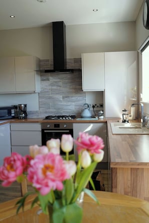 A modern kitchen with a stove, microwave, and coffee maker. There is a vase with flowers on the table. - 1 The Old Stables is a rural cottage with scenic countryside views. (Knitsley)