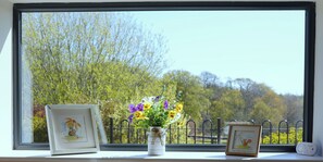 A window with a view of trees and a white vase with flowers on a windowsill. - 1 The Old Stables is a rural cottage with scenic countryside views. (Knitsley)
