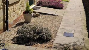 A row of stone buildings with a paved walkway, a green door, and a well-maintained garden with purple flowers. - 1 The Old Stables is a rural cottage with scenic countryside views. (Knitsley)