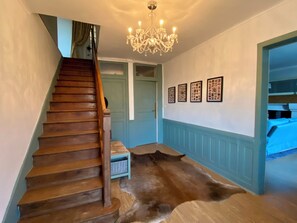A staircase with wooden steps, a chandelier, a blue door, and framed pictures on the wall. - Country house - Sleeps 8 (Jublains)