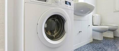 A front-loading washing machine in a bathroom with a toilet and a sink.