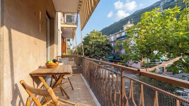 Een balkon met een tafel en stoelen, uitzicht op een berg, en een gebouw met balkons.