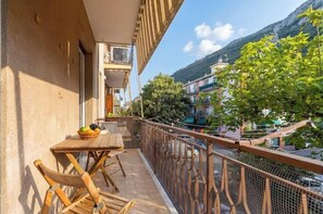 A balcony with a table and chairs, a view of a mountain, and a building with balconies. - Hostdomus - Two-room apartment on the village (Finale Ligure)