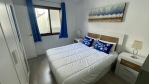Een slaapkamer met een bed, nachtkastje, lamp, raam met gordijnen en een schilderij aan de muur.
